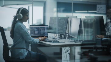 Woman software developer sitting at a desk wearing headphones.
